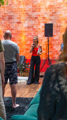 Christina Weber standing solo with microphone against the glowing salt wall backdrop